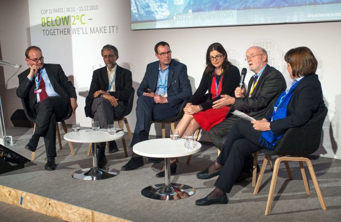 Diskussionsrunde zu den Herausforderungen an eine moderne Klimaforschung beim BMBF-Side Event „From Research to Decision Making” V.l.n.r.: Podiumsdiskussion mit Ottmar Edenhofer, PIK, Christoph Bals, Germanwatch, Gregor Laumann, DLR-PT, Grit Martinez, Ecologic Institut und Vera Stercken, Bundesforschungsministerium.
Auf dem BMBF-Side Event „From Research to Decision Making”, welches am 03.12.2015 im Rahmen der 21. Klimakonferenz (COP21) in Paris stattfand, eröffnete Karl Eugen Huthmacher (Leiter der Abteilung 7 „Zukunftsvorsorge – Forschung für Grundlagen und Nachhaltigkeit“, BMBF) die Diskussion zu den Herausforderungen an eine moderne Klimaforschung.
Im Podiumsgespräch boten Prof. Ottmar Edenhofer (IPCC Co-chair AR5 WG III) und Prof. Hans-Otto Pörtner (IPCC Co-chair AR6 WG II) Einblicke in ihre Tätigkeiten an der Wissenschaft-Politik-Schnittstelle. Grit Martinez (Ecologic Institut) zeigt den Transfer von Klimawissen am Beispiel der BMBF-Fördermaßnahme Klimzug auf. Christoph Bals (Germanwatch) formulierte die Anforderungen an eine moderne Klimaforschung aus Sicht einer Entwicklungs- und Umweltorganisation, die sich für globale Gerechtigkeit und den Erhalt von Lebensgrundlagen einsetzt.“
