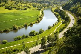 Das Foto zeigt einen Fluss mit einer Stra&szlig;e und gr&uuml;nen Wiesen.