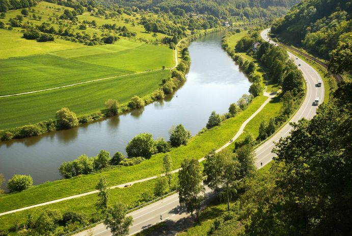 Das Foto zeigt einen Fluss mit einer Stra&szlig;e und gr&uuml;nen Wiesen.