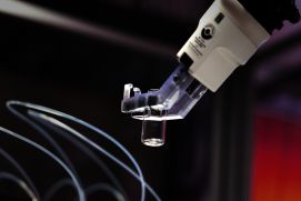 Ein Roboterarm bewegt einen leeren Probenbehälter präzise zwischen automatisierten Arbeitsstationen hin und her. 