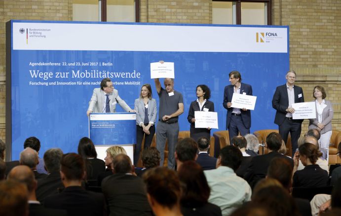 Einführung in die Workshops der Agendakonferenz "Wege zur Mobilitätswende" am 22. und 23. Juni 2017 in Berlin v.l.n.r.: Prof. Dr. Hans Liudger- Dienel (nexus | IBBA TU Berlin), Sarah Wutz (InnoZ), Dr. Weert Canzler (WZB), Dr. Angela Jain (nexus Institut), Christoph Henseler (nexus Institut | TU Berlin), Dr. Christian Hoffmann (InnoZ), Dr. Birgit Böhm (nexus Institut | TU Berlin)
Mobilität und urbaner Verkehr befinden sich derzeit in einem dynamischen Wandel. In den Städten entstehen zum einen vielfältige neue Mobilitätsdienstleistungen und Verkehrsangebote, zum anderen verändern sich Mobilitätsmuster und Rahmenbedingungen der Mobilität. Dieser Wandel der Mobilitätswelt erfordert eine verstärkte Einbindung der Forschung, um diesen Wandel mit zu gestalten. Das Bundesministerium für Bildung und Forschung (BMBF) führt daher im Jahr 2017 einen Agendaprozess „Nachhaltige urbane Mobilität" durch. Dieser erfolgt unter Mitwirkung des Bundesministeriums für Verkehr und digitale Infrastruktur (BMVI).
Im Rahmen dieses Prozesses diskutierten 300 Expertinnen und Experten aus Wissenschaft, Wirtschaft, Politik und Zivilgesellschaft auf der "Agendakonferenz: Wege zur Mobilitätswende" über Forschungs- und Umsetzungsbedarfe für eine nachhaltige Entwicklung von Mobilität in Städten.