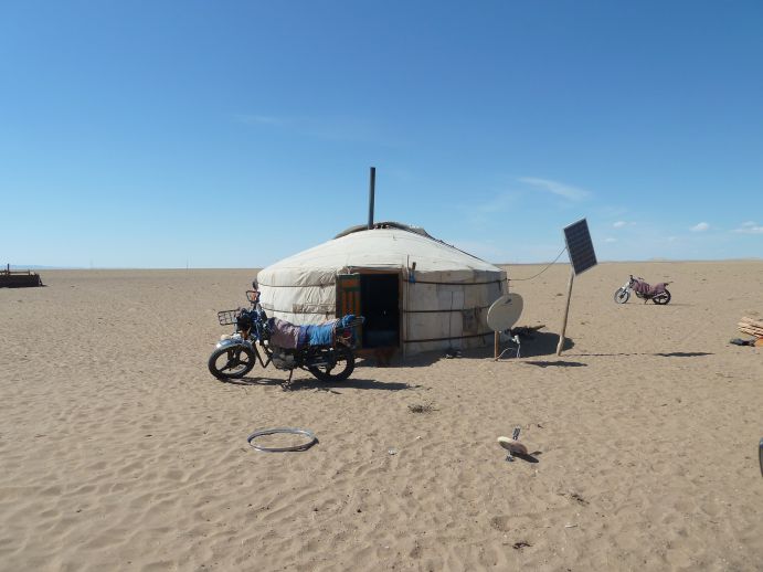 Das Foto zeigt eine Jurte mit einem Solarpanel in einer trockenen, flachen Landschaft der Mongolei.