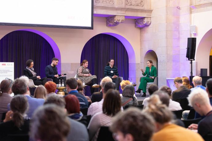 Teilnehmende verfolgen die Podiumsdiskussion und bringen eigene Fragen ein