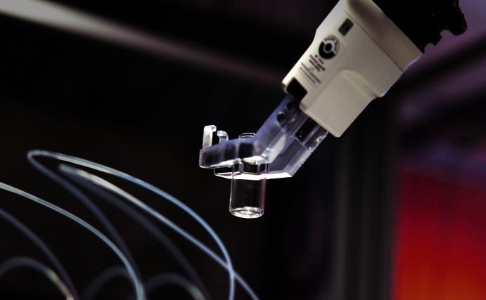 Ein Roboterarm bewegt einen leeren Probenbehälter präzise zwischen automatisierten Arbeitsstationen hin und her. 