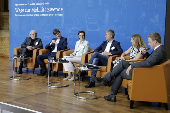 Podumsdiskussion Forschung und Innovation für eine nachhaltige urbane Mobilität v.l.n.r.: Prof. Dr. Andreas Knie (WZB/InnoZ), Prof. Dr. Achim Kampker (Deutsche Post DHL Group), Sybille Benning (MdB, Fraktion CDU/CSU), Dieter Janecek (MdB, Fraktion Bündnis 90/Die Grünen), Sabine Nallinger (Stiftung 2°) und Moderator Peter Schwierz (Chefredakteur, electrive.net).
Mobilität und urbaner Verkehr befinden sich derzeit in einem dynamischen Wandel. In den Städten entstehen zum einen vielfältige neue Mobilitätsdienstleistungen und Verkehrsangebote, zum anderen verändern sich Mobilitätsmuster und Rahmenbedingungen der Mobilität. Dieser Wandel der Mobilitätswelt erfordert eine verstärkte Einbindung der Forschung, um diesen Wandel mit zu gestalten. Das Bundesministerium für Bildung und Forschung (BMBF) führt daher im Jahr 2017 einen Agendaprozess „Nachhaltige urbane Mobilität" durch. Dieser erfolgt unter Mitwirkung des Bundesministeriums für Verkehr und digitale Infrastruktur (BMVI).
Im Rahmen dieses Prozesses diskutierten 300 Expertinnen und Experten aus Wissenschaft, Wirtschaft, Politik und Zivilgesellschaft auf der "Agendakonferenz: Wege zur Mobilitätswende" über Forschungs- und Umsetzungsbedarfe für eine nachhaltige Entwicklung von Mobilität in Städten.