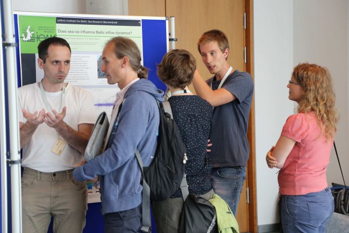Wissenschaftler diskutieren ihre Ergebnisse bei der BSSC-Postersession. Fünf junge Leute stehen vor Stellwänden, an die wissenschaftliche Poster gepinnt sind, die Graphen, Formeln und Text zeigen.