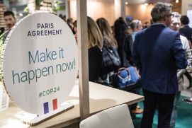 Aufsteller mit der Aufschrift "Paris Agreement - Make it happen now!" auf der Weltklimakonferenz 2018, im Hintergrund Menschen, die sich unterhalten (Friedemann Call / DLR Projektträger)