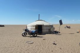 Das Foto zeigt eine Jurte mit einem Solarpanel in einer trockenen, flachen Landschaft der Mongolei.
