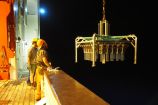 Eine große Maschine, die Meeresbodenproben sammelt, wird langsam vom Deck eines Forschungsschiffes runtergelassen.