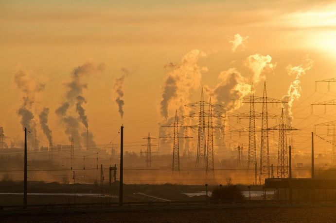 Die Erfordernisse und das Potenzial für Emissionseinsparungen sollen im Projekt EcoEff mit Hilfe von Methoden der Effizienzmessung quantifiziert werden. Sonnenaufgang mit Strommasten, rauchenden Schlote im Hintergrund und Smog allgegenwärtig.