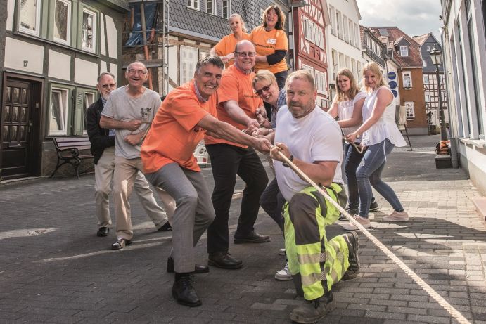 Männer und Frauen in einer Altstadt ziehen an einem Strang. 