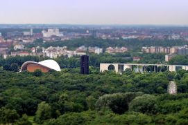 Städtiche Grünanlage mit einigen Gebäuden zwischendrin und der Stadt im Hintergrund.