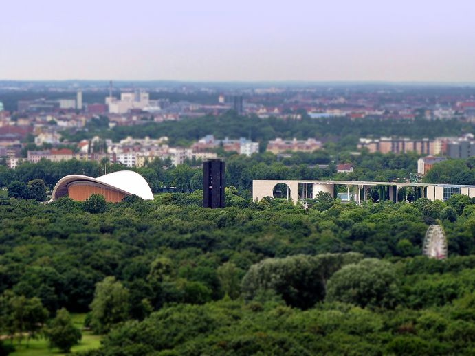 Städtiche Grünanlage mit einigen Gebäuden zwischendrin und der Stadt im Hintergrund.