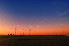 Strommasten über Feldern mit Industrieanlagen im Hintergrund
