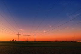 Strommasten über Feldern mit Industrieanlagen im Hintergrund