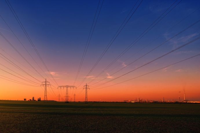 Dank des Kopernikus-Projekts SynErgie kann die Industrie heute schon flexibel auf unterschiedliche Lasten im Netz reagieren. Strommasten über Feldern mit Industrieanlagen im Hintergrund