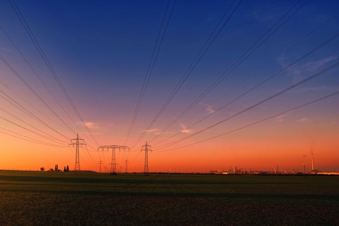 Strommasten über Feldern mit Industrieanlagen im Hintergrund