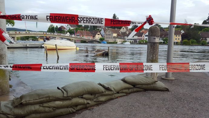 Feuerwehr-Sperrzone am Ufer eines Flusses mit Häusern im Hintergrund