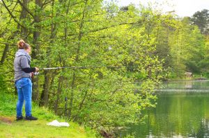 Anglerinnen und Angler sind bereit, sich aktiv für den Artenschutz am Gewässer einzusetzen. Anglerin steht an einem Baggersee mit einer Angelrute.