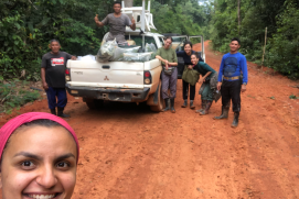 Tag der Tropenwälder - Selfie einer Forscherin im Amazonas mit einem Pick-up Wagen und einer Gruppe von Menschen im Hintergrund.