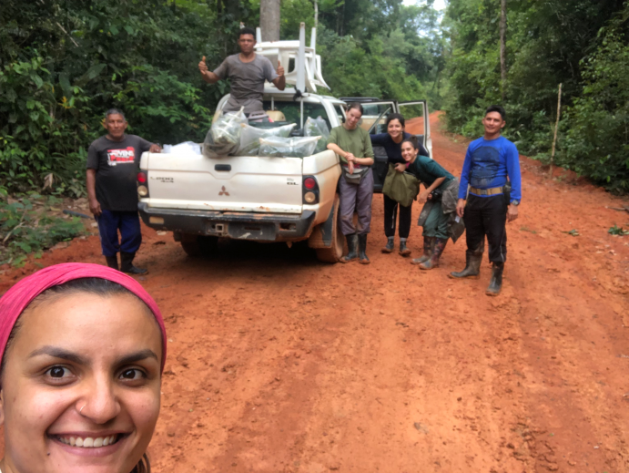 Tag der Tropenwälder - Selfie einer Forscherin im Amazonas mit einem Pick-up Wagen und einer Gruppe von Menschen im Hintergrund.