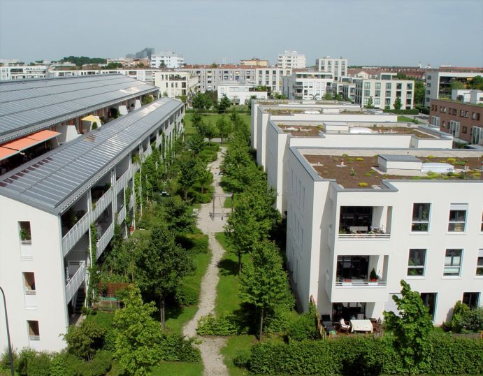 Steigender Bedarf an Wohnflächen steht in Konkurrenz zu Grün- und Freiflächen, die für eine klimaresiliente Stadtentwicklung dringend nötig sind. Wohnsiedlung in München mit Park und begrünten Dächern.