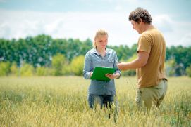 Landwirt und Expertin stehen im Feld und machen Notizen