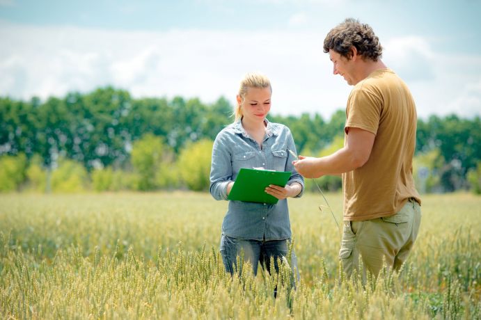 Landwirt und Expertin stehen im Feld und machen Notizen