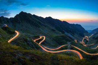 Berglandschaft mit Serpentinenstraßen, die durch lange Belichtung die Rückleuchten und Scheinwerfer fahrender Autos als Streifen zeigen.