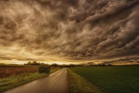 Panoramabild mit Feldern, Straße und Gewitterwolken im Sonnenuntergang