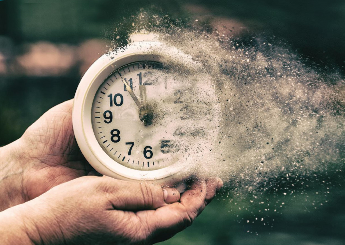 Zeit und Nachhaltigkeit Uhr, die von einem Paar Hände gehalten wird und im Sand verfliegt