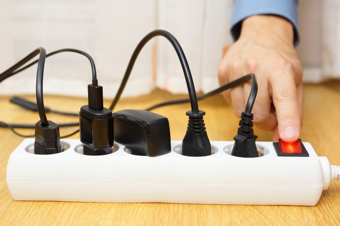 Viele Elektrogeräte verbrauchen Strom. Das Abschalten der Mehrfachsteckdose hilft Energie einzusparen. Eine Hand schaltet drückt auf den Schalter einer Mehrfachsteckdose