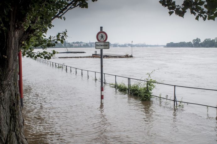Hochwasser oder Überschwemmungen durch Starkregen treten in Deutschland immer häufiger auf Überflutete Flussufer mit Hochwasserwarnschild