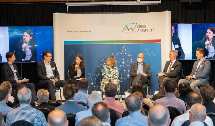 Diskussionsrunde zum Thema „Wiederaufbau, Resilienz und Modellansätze: Herausforderungen und Chancen“: Wilhelm Schulz (Moderation, Landkreis Ahrweiler), Prof. Jörn Birkmann (Sprecher des KAHR-Projekts, Universität Stuttgart), Cornelia Weigand (Landrätin, Landkreis Ahrweiler), Katrin Eder (Klimaschutzministerin, Ministerium für Klimaschutz, Umwelt, Energie und Mobilität), Prof. Holger Schüttrumpf (Sprecher des KAHR-Projekts, RWTH Aachen), Achim Blindert (Allgemeiner Vertreter des Landrats, Landkreis Euskirchen), Mario Brandenburg (Parlamentarischer Staatsekretär, Bundesministerium für Bildung und Forschung)[von links nach rechts]